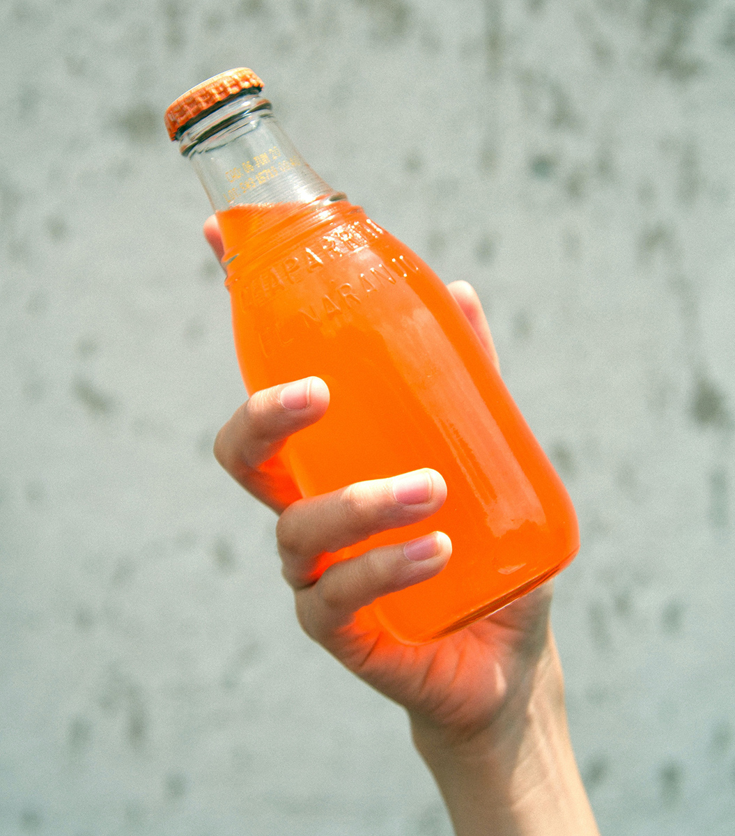 A woman's hand holding a bottle of orange-flavored soda