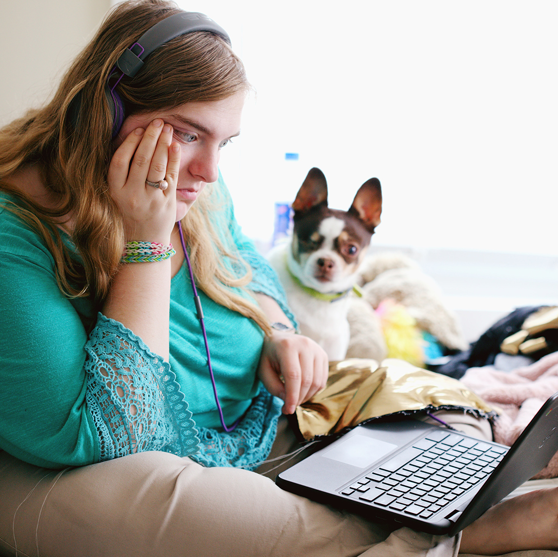 Overweight woman typing on her laptop as she sits on her bed with her dog