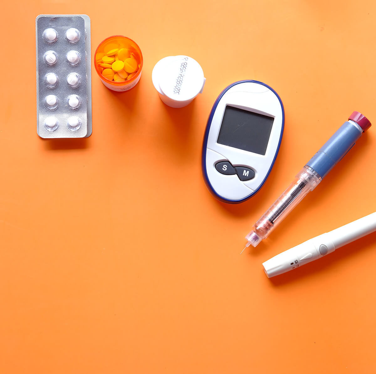 a selection of heart medication, insulin pens, blood sugar monitor and diabetic medication placed on a table