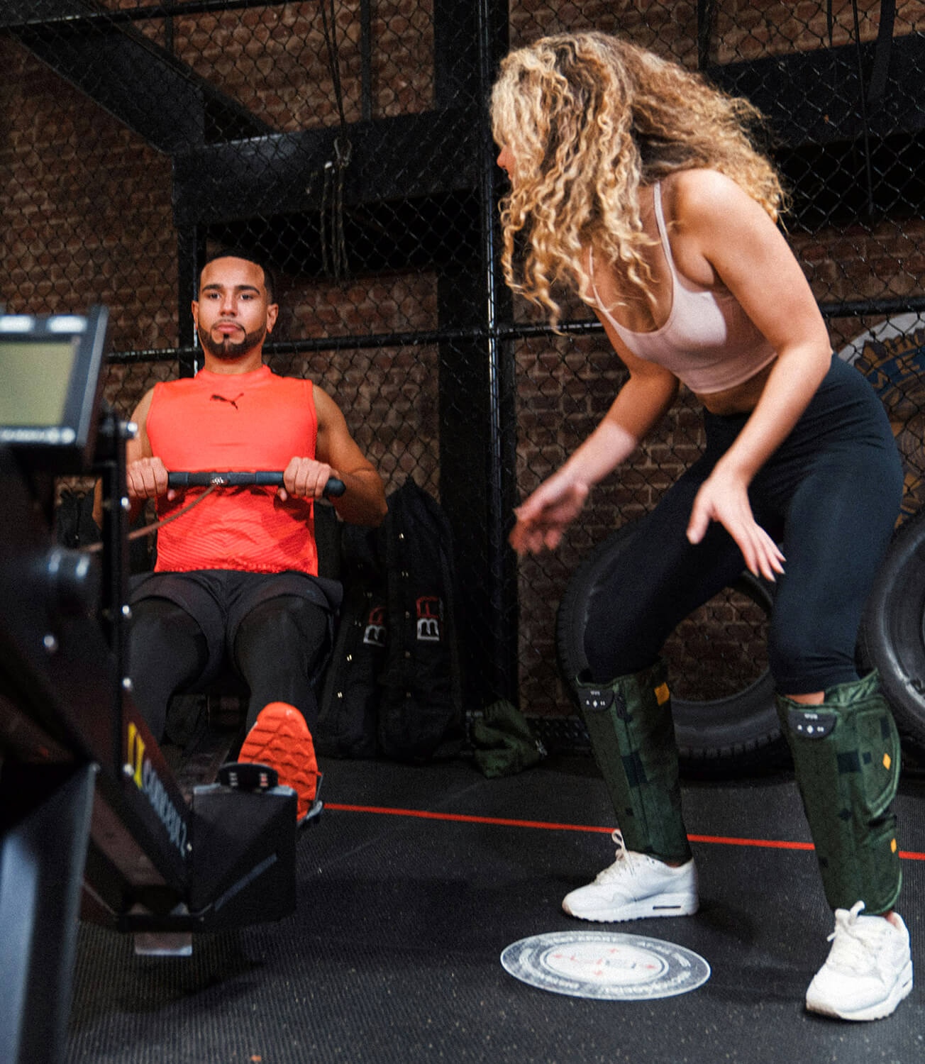 A woman encouraging her male friend as he exercises in the gym